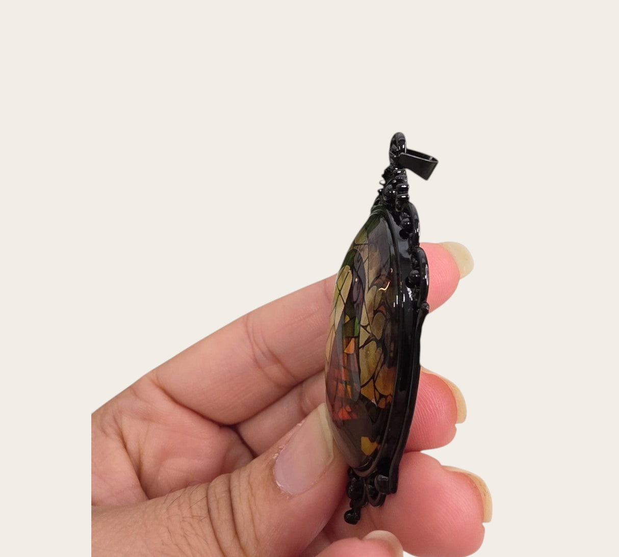 My Magic Place Shop witch hat cameo pendant with a black filigree frame held in a hand, side view.