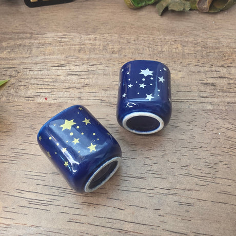 Two small ceramic cups decorated with white and gold stars on a dark blue background, arranged on a wooden tabletop.