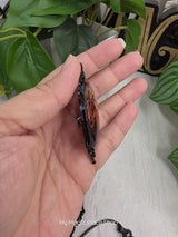 My Magic Place Shop oval witch glass cabochon pendant in an ornate black metal frame, side view held in hand.