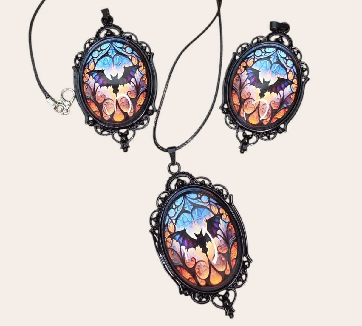 oval gothic bat pendants with stained glass style cabochons on a wooden display base.